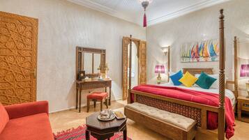 A traditional room with a four-poster bed, a wooden desk, a red armchair, and a patterned rug.