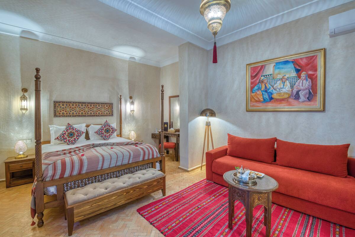 Un dormitorio con cama con dosel, un sofá rojo y un cuadro en la pared.