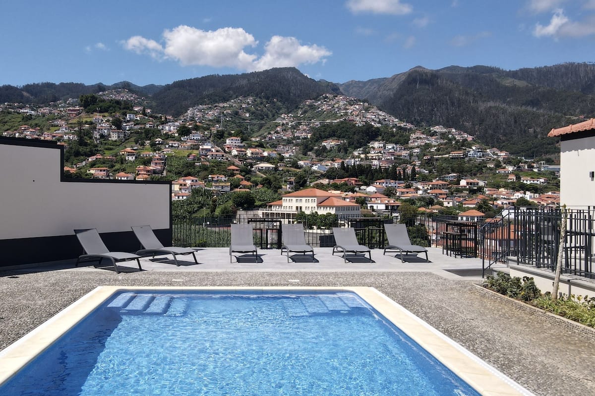 Ein Pool auf dem Dach mit Liegestühlen und Blick auf eine Stadt am Hang.