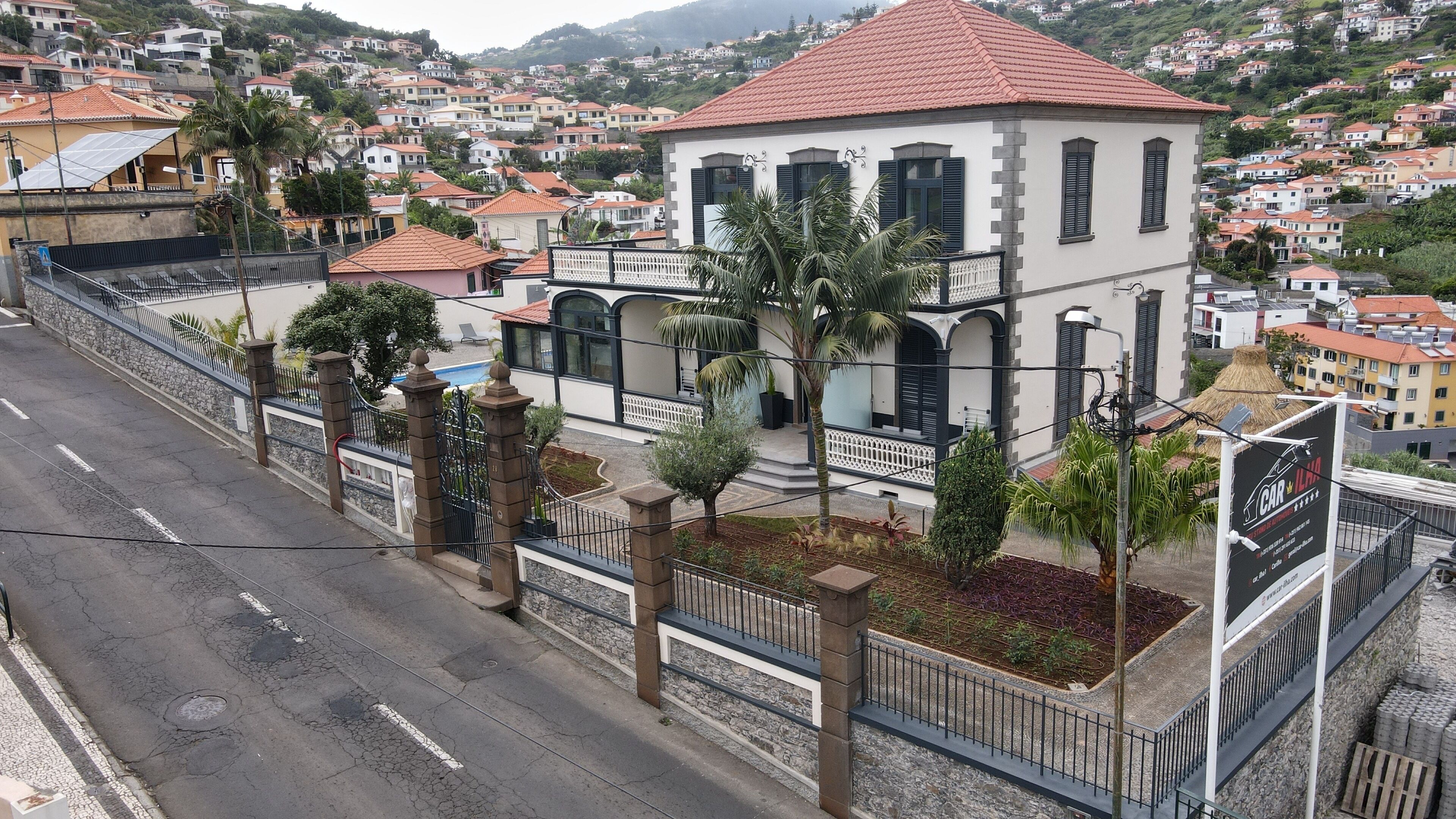 A white building with a red roof, surrounded by a fence and small trees.