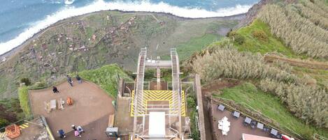 An aerial view of a coastal facility with a staircase leading to a viewing platform, surrounded by greenery and overlooking the ocean.