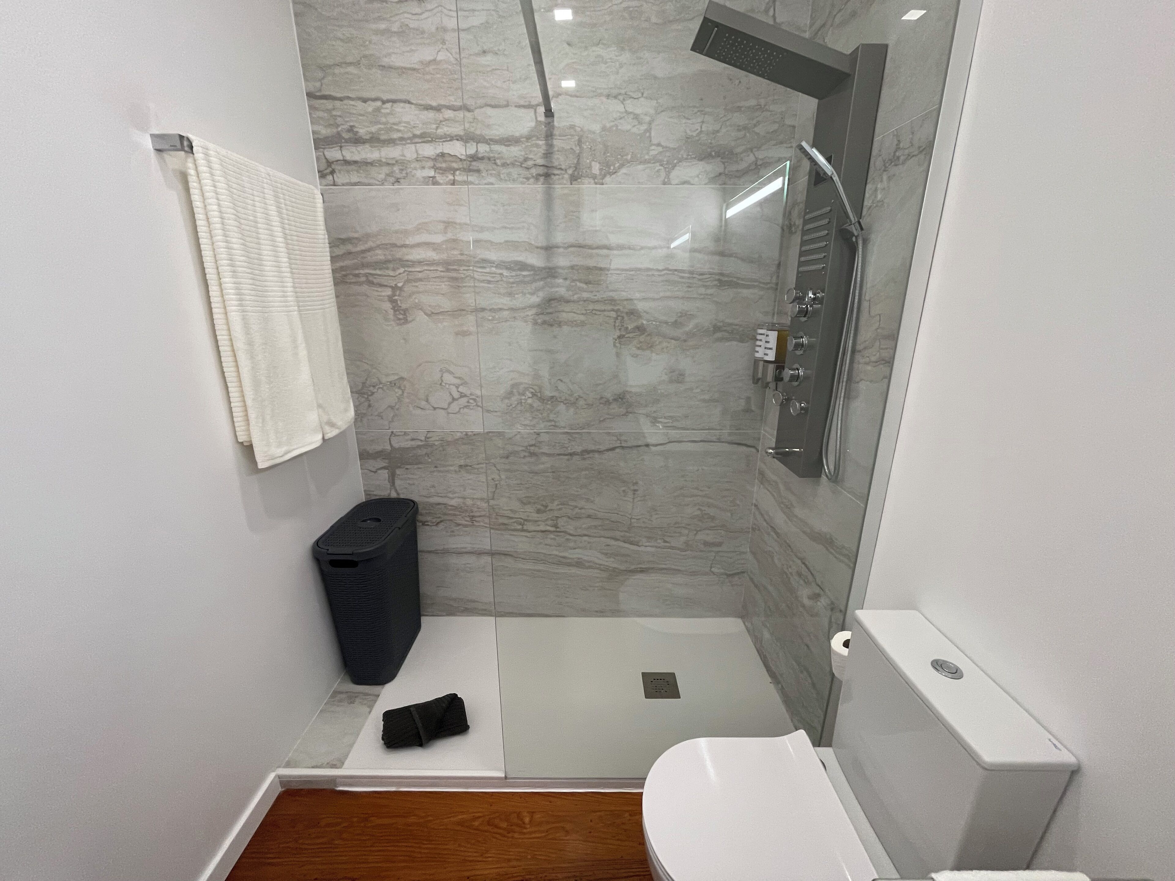 A modern bathroom with a glass-enclosed shower, a white toilet, and a black trash bin.