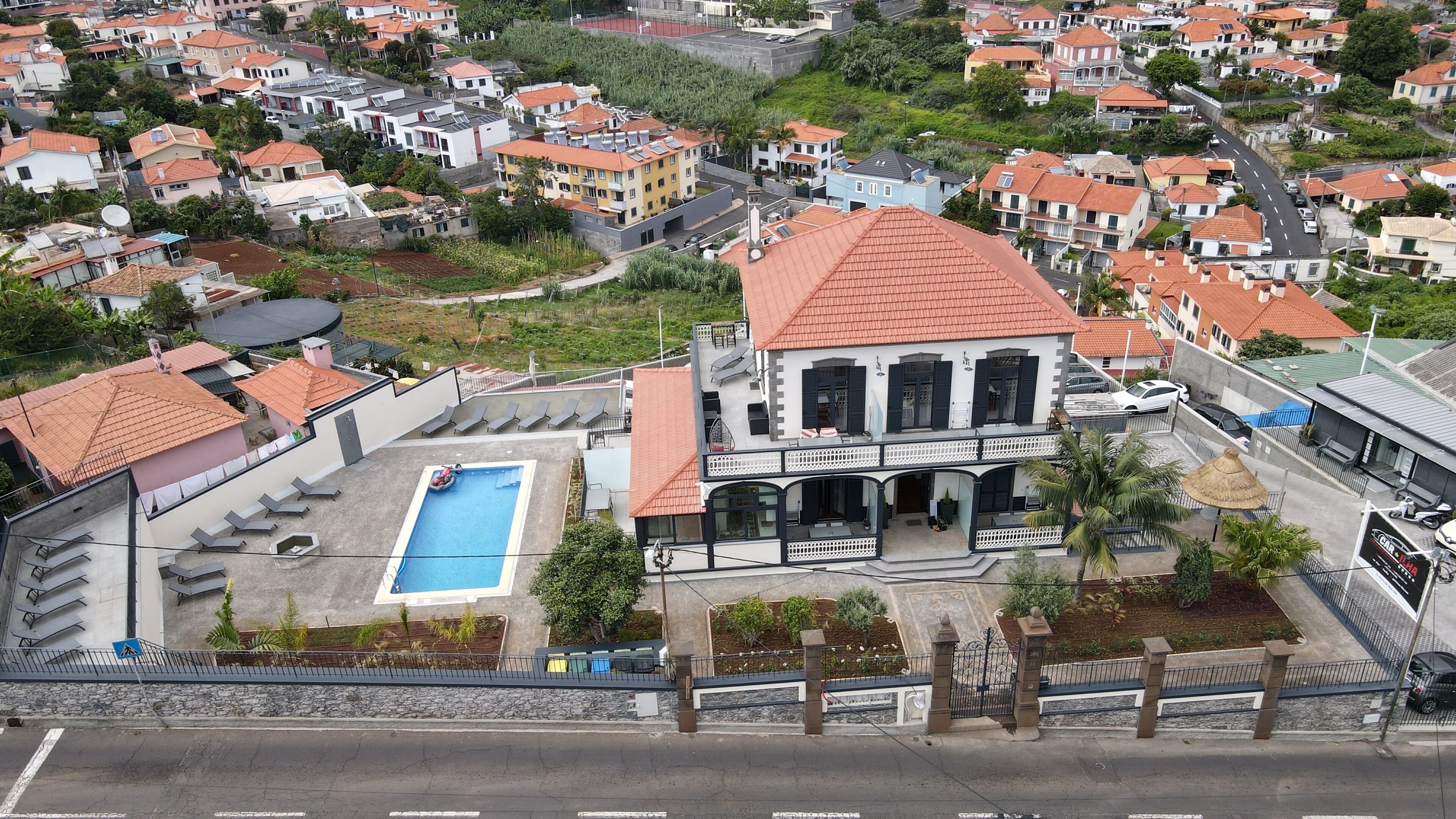 Zona residencial con una casa grande que cuenta con piscina, varios balcones y entrada protegida por un portón.