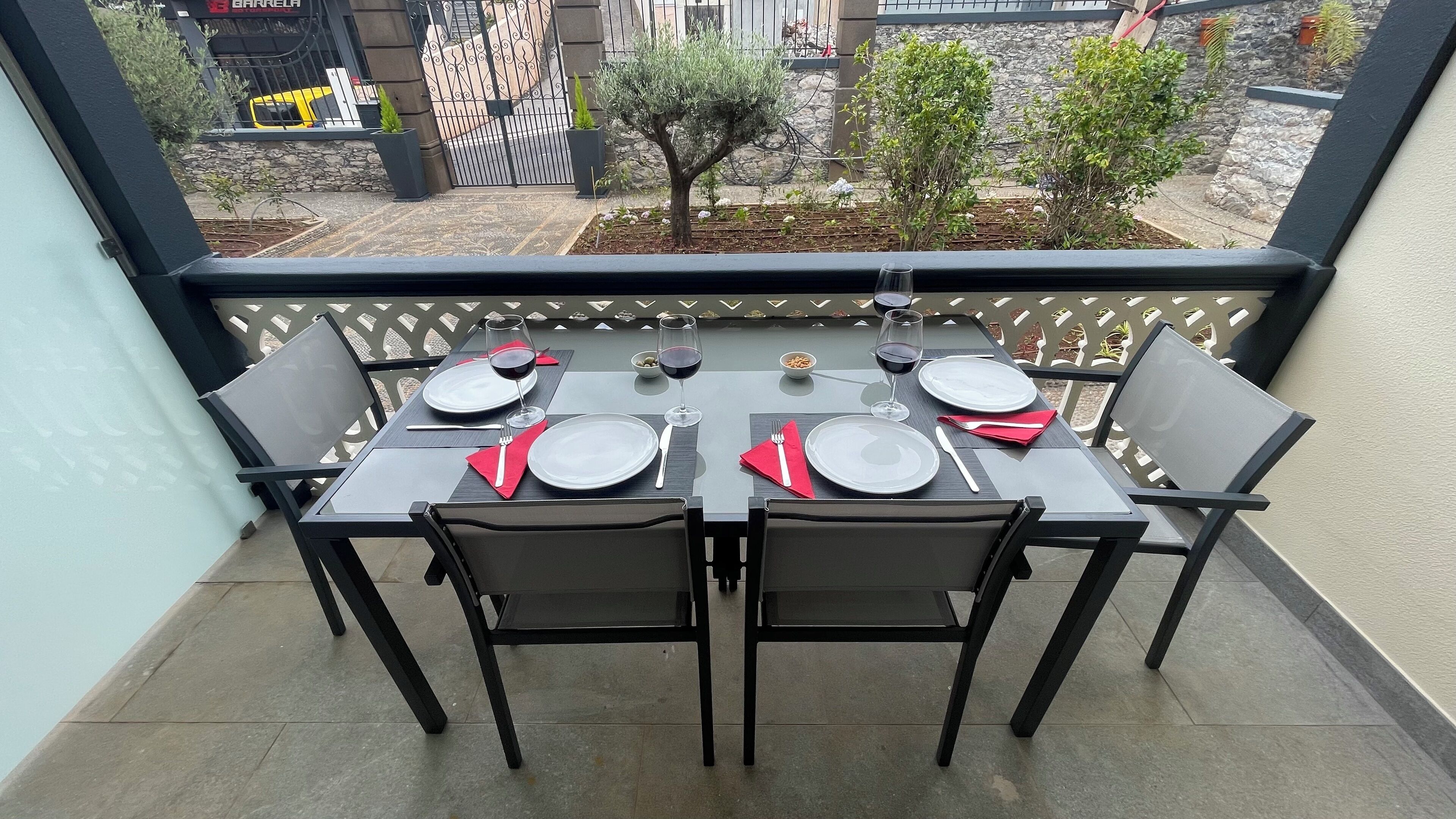 Une table de balcon, dressée avec des assiettes, des verres et des couverts, entourée de chaises.