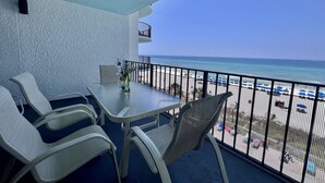 Ein Balkon mit Tisch und Stühlen mit Blick auf einen Strand mit Sonnenschirmen.
