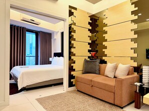 A hotel room with a bed, a sofa, a patterned rug, and a wall with a geometric design.