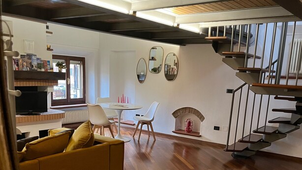 A modern living room with a wooden floor, a sofa, a dining table with chairs, a fireplace, and a staircase. - Loft Albinelli in the heart of Modena (Modena)