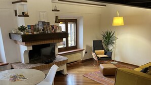 A modern living room with a wooden floor, a round dining table, white chairs, a sofa, and a TV on a built-in shelf. - Loft Albinelli in the heart of Modena (Modena)