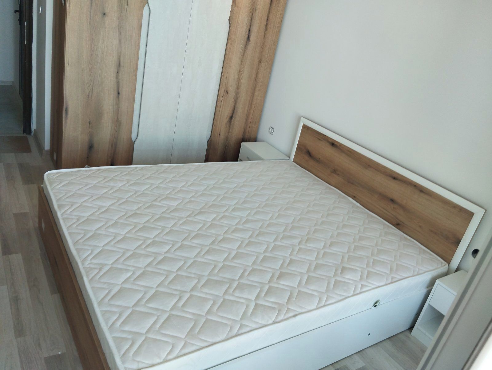 Une chambre avec un lit simple, une tête de lit en bois, un matelas blanc et une petite table de chevet.