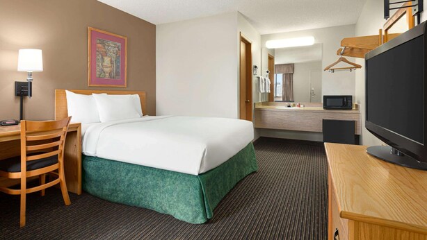 A hotel room with a bed, desk, chair, TV, and a bathroom with a mirror and towel rack. - Travelodge By Wyndham Wellington (Wellington)