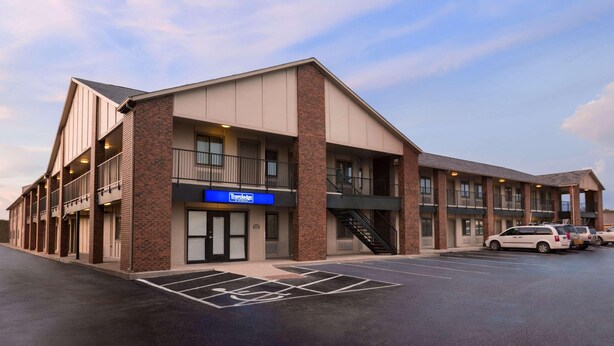 A multi-story hotel with a brick facade, a visible entrance, and a parking lot with marked handicapped spaces. - Travelodge By Wyndham Wellington (Wellington)