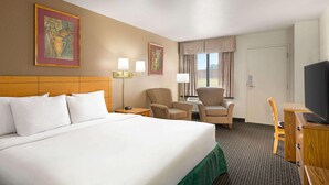 A hotel room with a large bed, two armchairs, a desk, a television, and artwork on the walls. - Travelodge By Wyndham Wellington (Wellington)