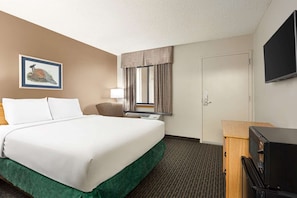 Una habitación de hotel con una cama, un escritorio, un televisor, una puerta y una ventana con cortinas.