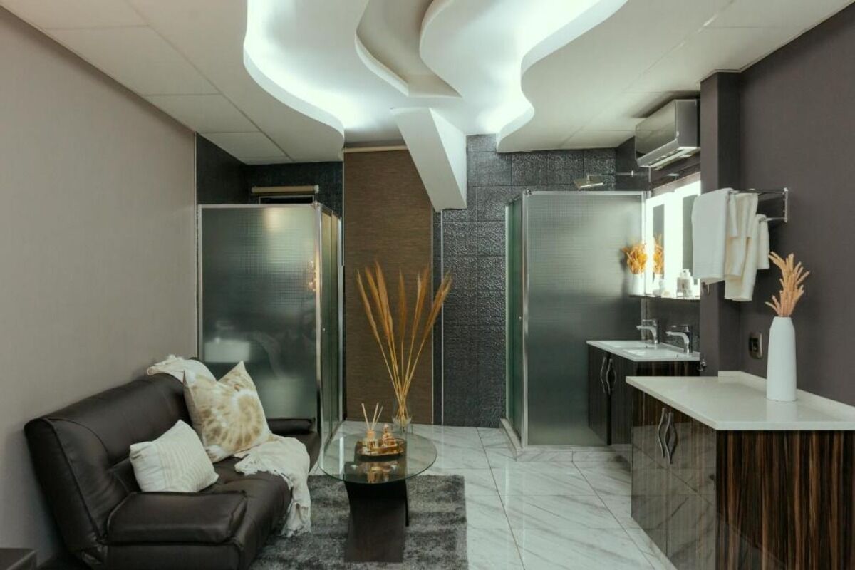 Una sala moderna con un sofá de cuero oscuro, una mesa de centro de vidrio y un jarrón decorativo. Se ve un área de cocina con una encimera blanca y una estufa empotrada al fondo.