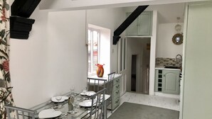 A dining area with a glass table set for four, a window with a view, and a kitchen area with a sink and cabinets. - Charming 2-bed Apartment in Waterloo, Liverpool (Liverpool)