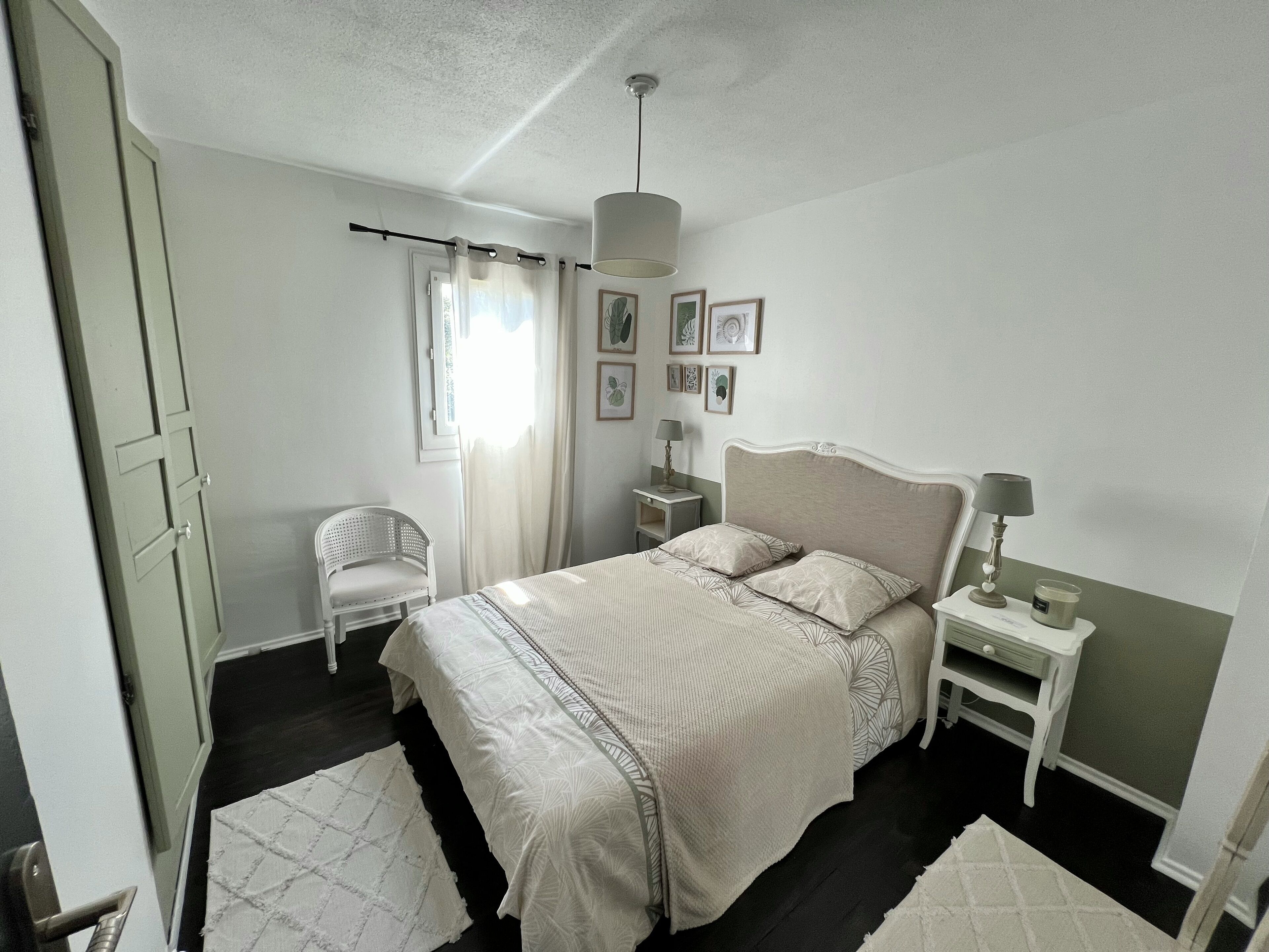 A bedroom with a bed, a chair, a nightstand, a lamp, and a window with curtains.
