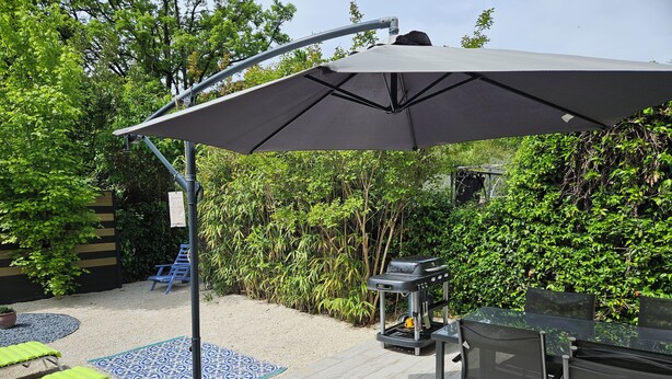 Un espace patio équipé d’un barbecue, de sièges d’extérieur et d’un grand parasol pour créer de l’ombre.
