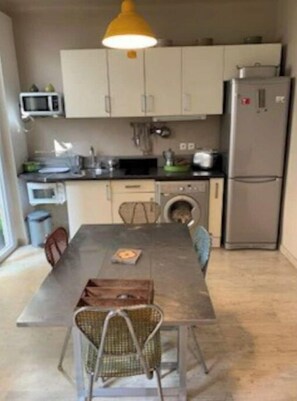 A compact kitchen with a dining table, chairs, a microwave, a refrigerator, and a washing machine.