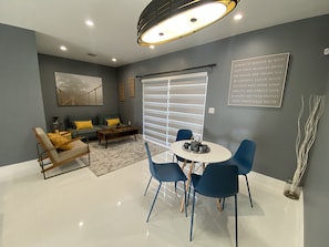 Una sala moderna con un sofá gris, sillas azules, una mesa de centro y una mesa de comedor.