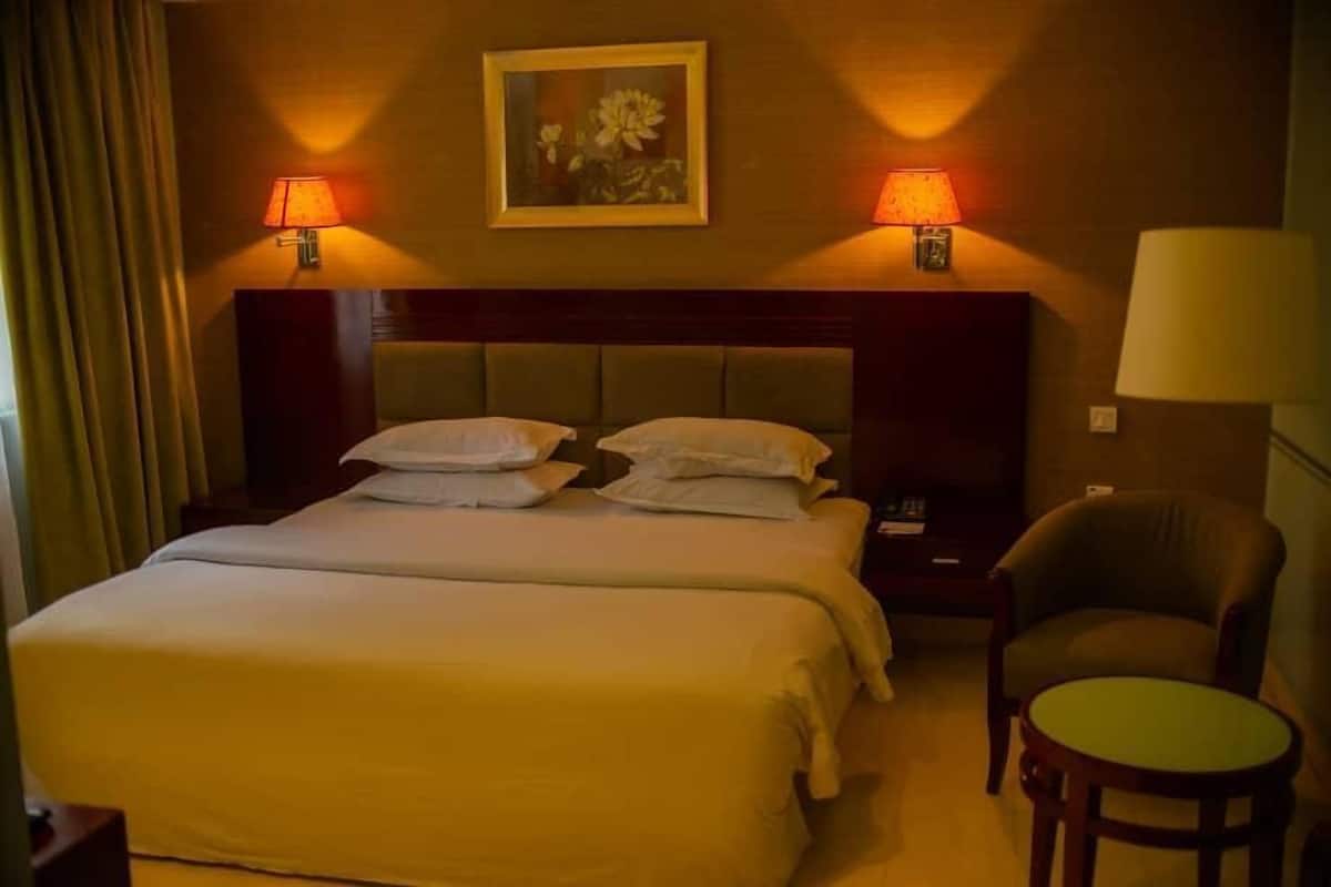 A hotel room with a large bed, two bedside lamps, a chair, and a small table.