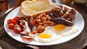 Un plato de comida para el desayuno con huevos, salchichas, frijoles, tostadas y tocino.