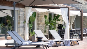 A sunlit outdoor lounge area with reclining chairs, a table, and umbrellas providing shade.