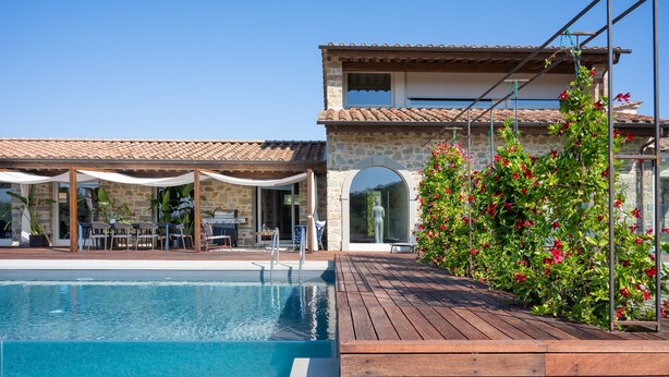 A pool area with a wooden deck, stone walls, and a covered seating area.