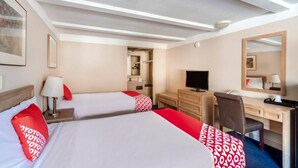 Une chambre d’hôtel avec deux lits, un bureau, une chaise, une télévision et une armoire.