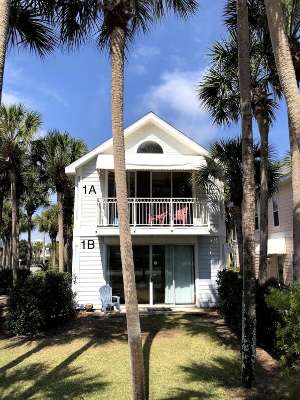 A two-story building with a balcony on the upper floor, surrounded by palm trees.