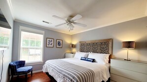 Ein Schlafzimmer mit einem Bett, einem Sessel, einem Deckenventilator, einem Fenster und einer Wandlampe.