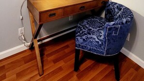 Ein Holztisch mit einer Lampe, ein blaues, gemustertes Stuhl und drei gerahmte Bilder an der Wand.
