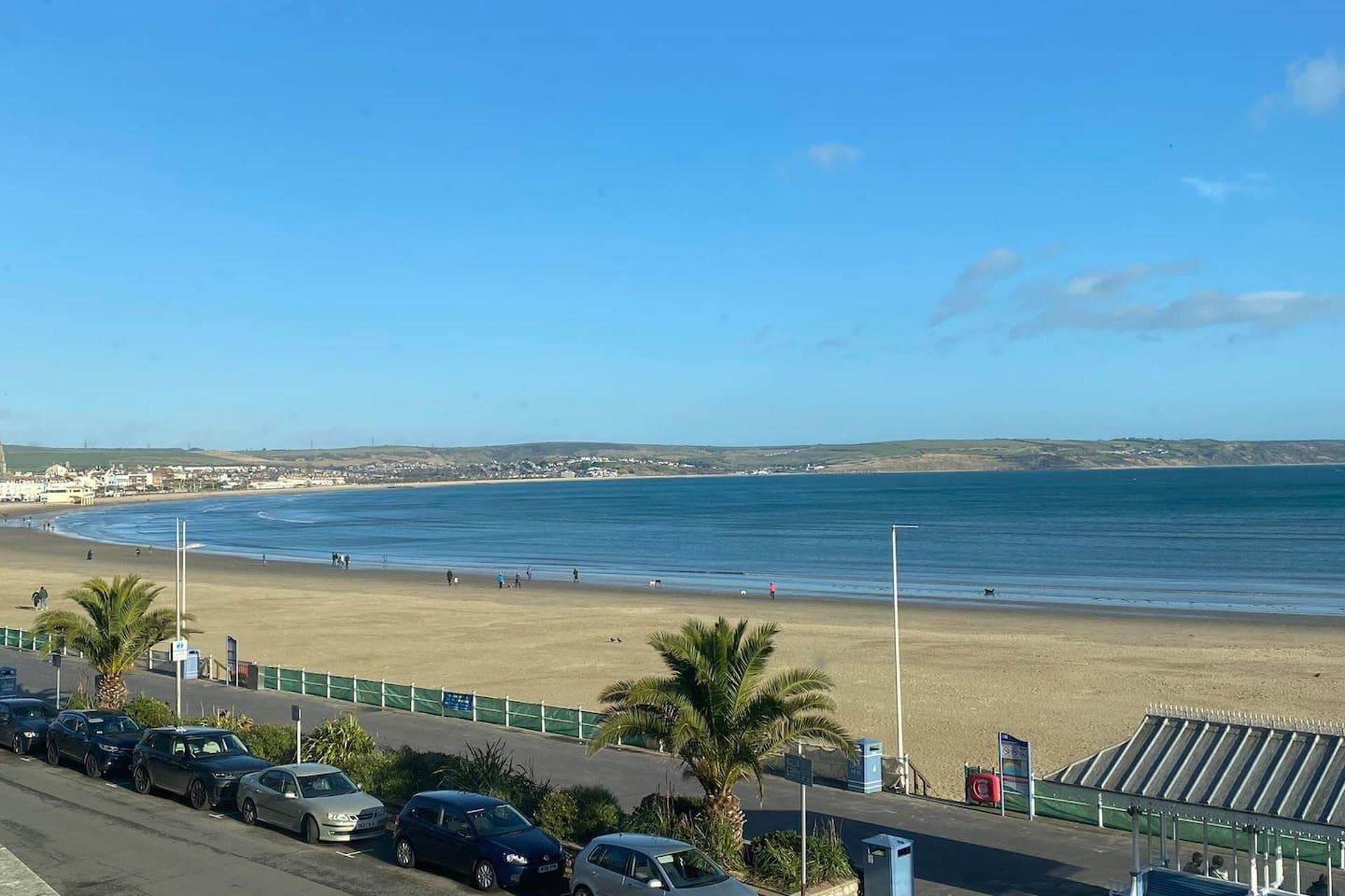 A beach with a parking lot and a road in the foreground.