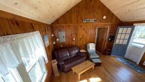 A cozy cabin interior with a wooden ceiling, a brown leather sofa, a light blue armchair, and a wooden coffee table.
