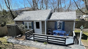 A small house with a porch, a table, and chairs, surrounded by a fenced yard.