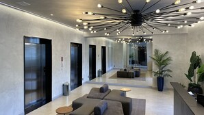 Eine moderne Lobby mit einer zentralen Sitzgruppe, mehreren Aufzügen und einer Deckenleuchte.