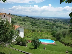 A villa with a swimming pool, surrounded by lush greenery and a view of distant hills.