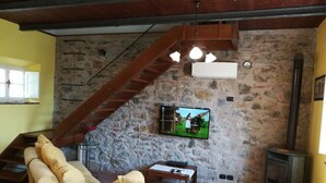 Ein gemütliches Wohnzimmer mit Steinwand, einer Holztreppe, einem Fernseher und einem Kamin.