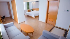Hotellihuone, jossa on sänky, oleskelualue sohvineen ja pöytineen sekä ovi, joka johtaa toiseen huoneeseen.