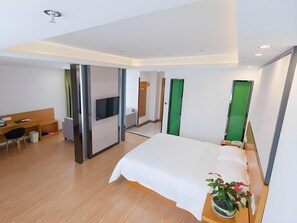 Ett modernt hotellrum med en säng, ett skrivbord, en stol, en tv och en grön dörr.