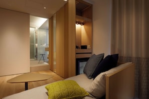 A modern room with a sofa, a small table, and a built-in bench. There is a glass door leading to a bathroom, and a small table with a chair is visible in the background. - Tsuki Tokyo (Tokyo)