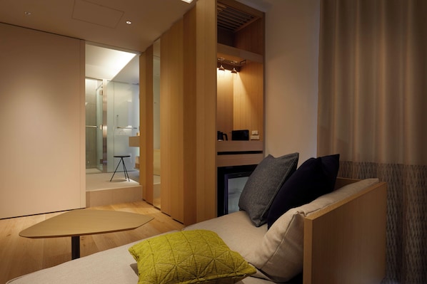 A modern room with a sofa, a small table, and a built-in bench. There is a glass door leading to a bathroom, and a small table with a chair is visible in the background. - Tsuki Tokyo (Tokyo)