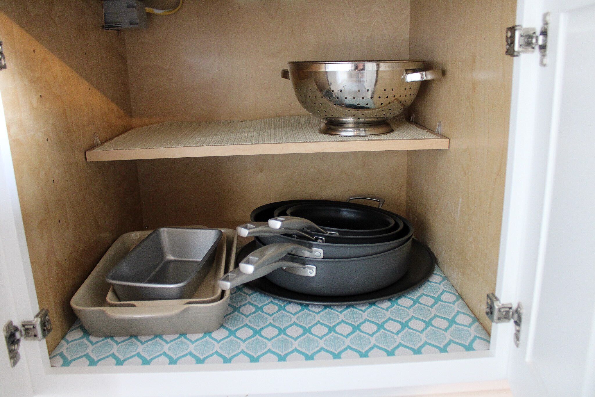 A compact kitchen with a metal colander on a shelf, a frying pan, and a baking tray on the counter.