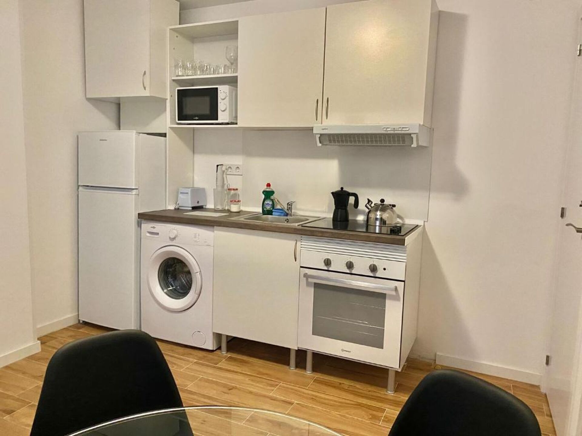 Una cucina compatta con lavatrice, forno a microonde, forno e un piccolo piano di lavoro con bollitore e macchina da caffè.