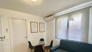 A room with a blue sofa, a glass table with four chairs, two framed artworks on the wall, and a door with a keypad lock.