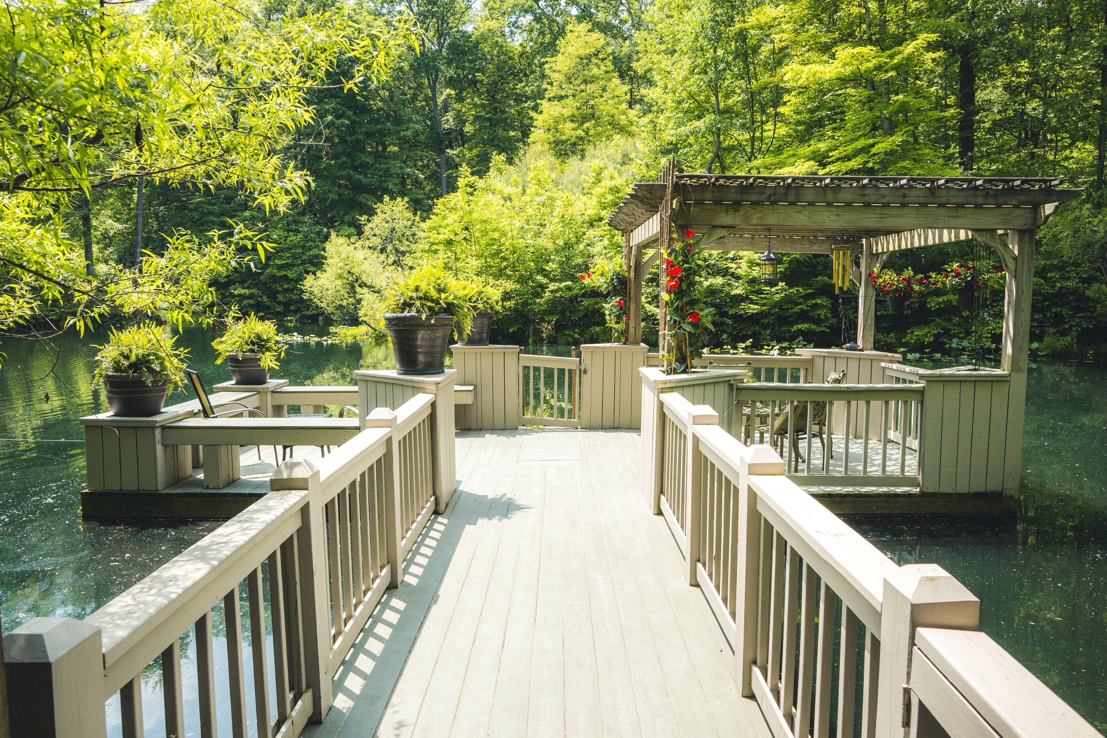 A wooden deck leading to a gazebo over a body of water, surrounded by lush greenery.