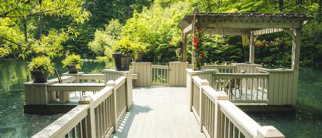 A wooden deck leading to a gazebo over a body of water, surrounded by lush greenery.