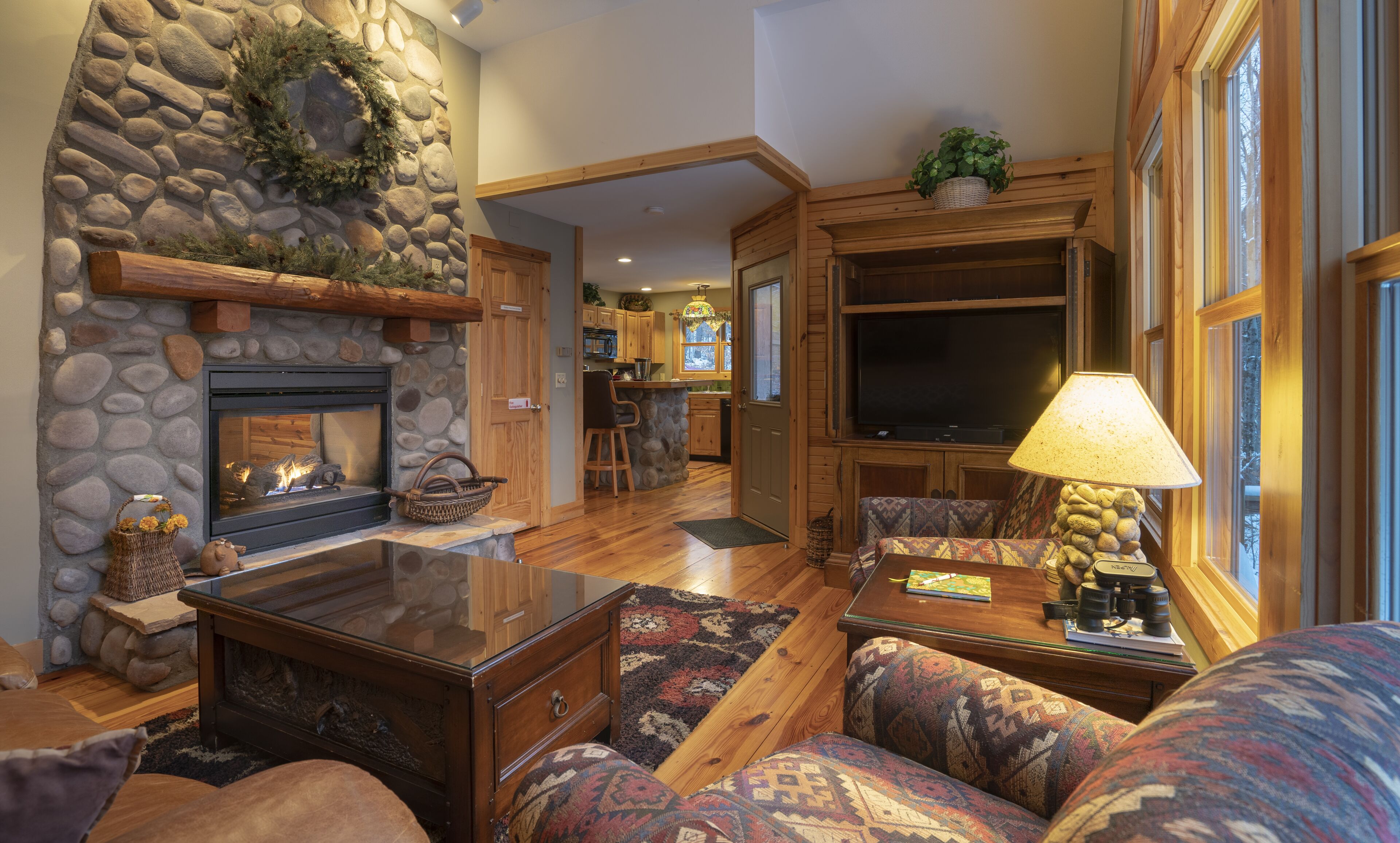 A cozy living room with a stone fireplace, wooden furniture, and a television.