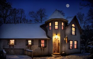 A snow-covered house with multiple windows and a flag, under a night sky with a visible moon. - Cherry Ridge Retreat (New Plymouth)