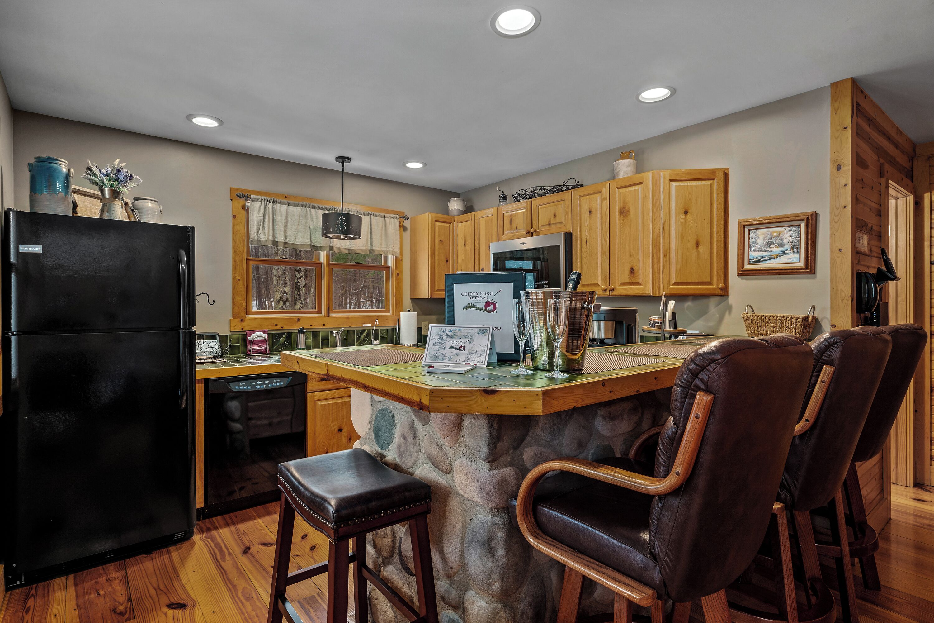 A kitchen with wooden cabinets, a black refrigerator, a stone island, and leather bar stools.