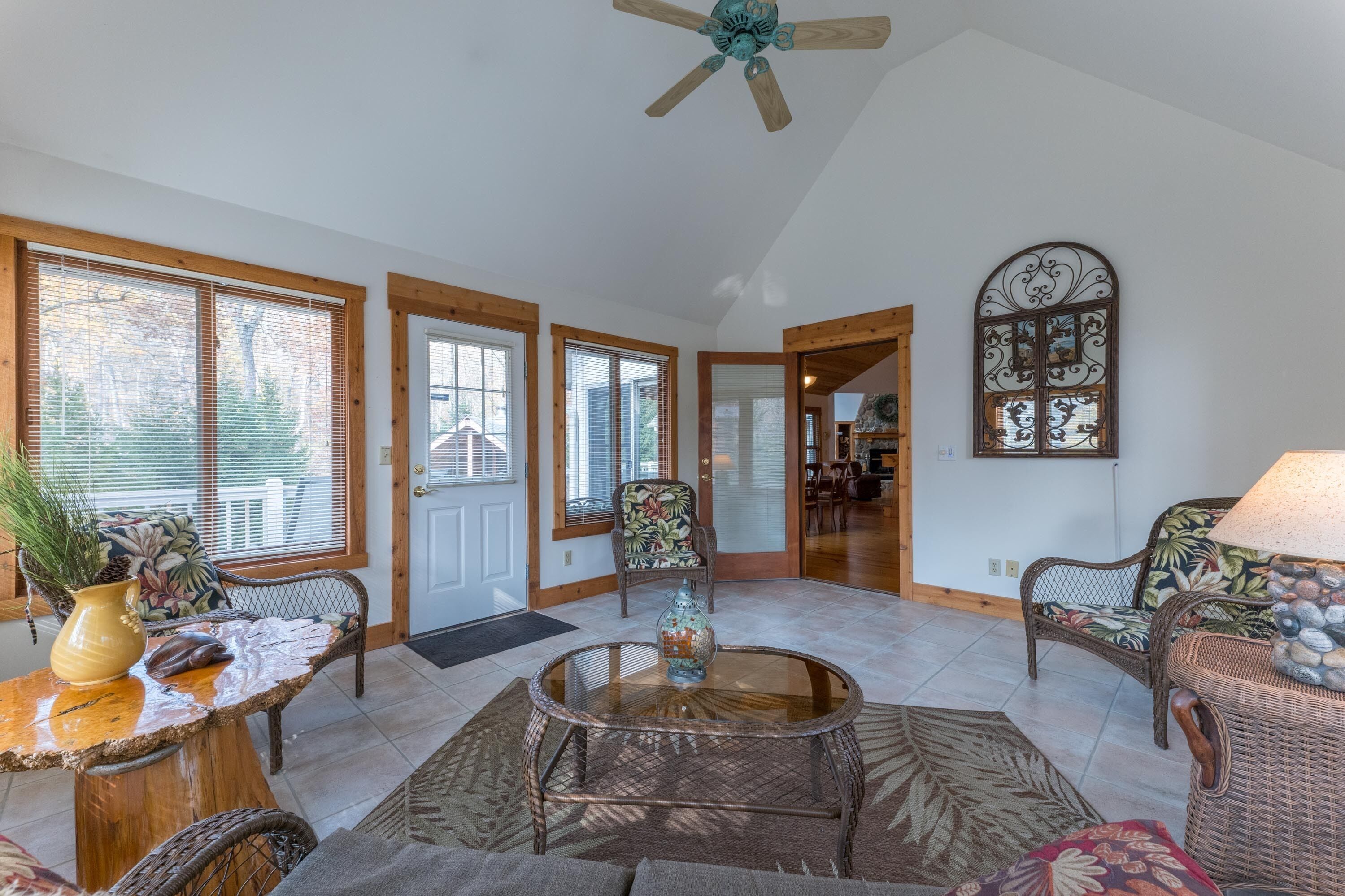 A spacious living room with a high ceiling fan, large windows, and a dining area visible in the background.